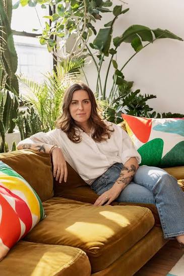 Amber Vittoria sitting on a mustard velvet sofa with colourful cushions