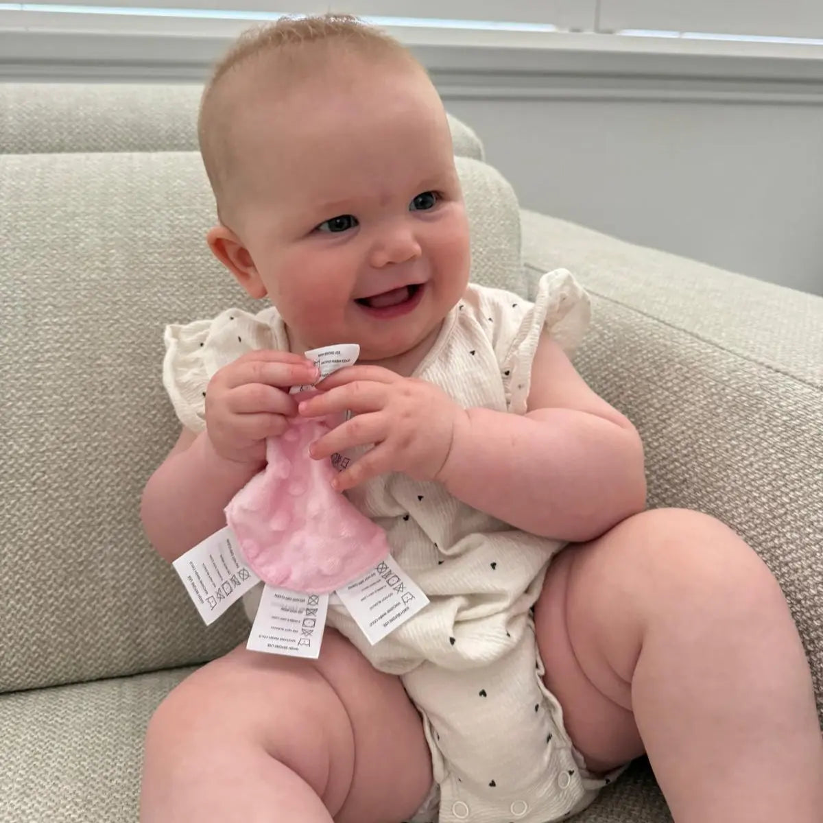 Baby smiling while holding pink sensory mini with soft fabric and multiple labels