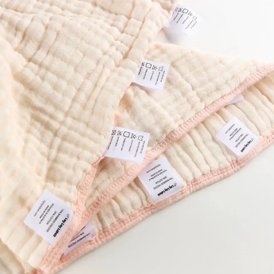 A folded pink-edged muslin tag blanket with labels along its edge